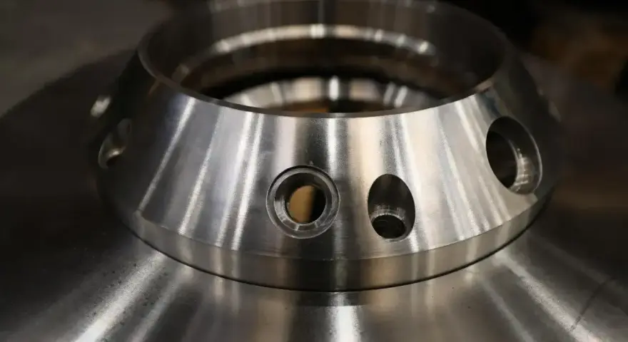 Metalowy element z otworami, przypominający kołnierz. To przykład precyzyjnej obróbki, która może być częścią procesu napawania.