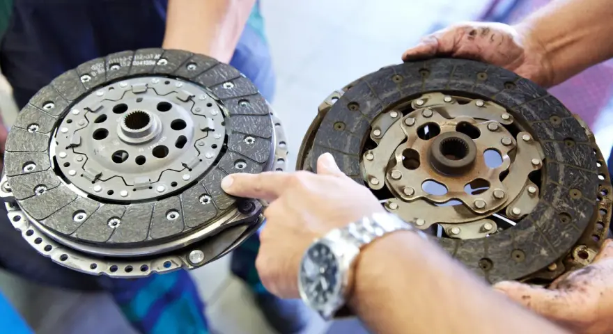 Dwie tarcze sprzęgła, jedna nowa, druga zużyta, prezentowane przez mechanika. Widać mechanizm sprzęgła samonastawne.