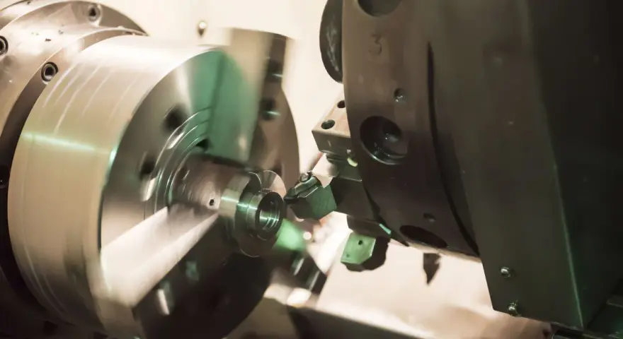 Precyzyjne toczenie aluminium na obrabiarce CNC. Metalowy element obraca się, a narzędzie nadaje mu kształt.