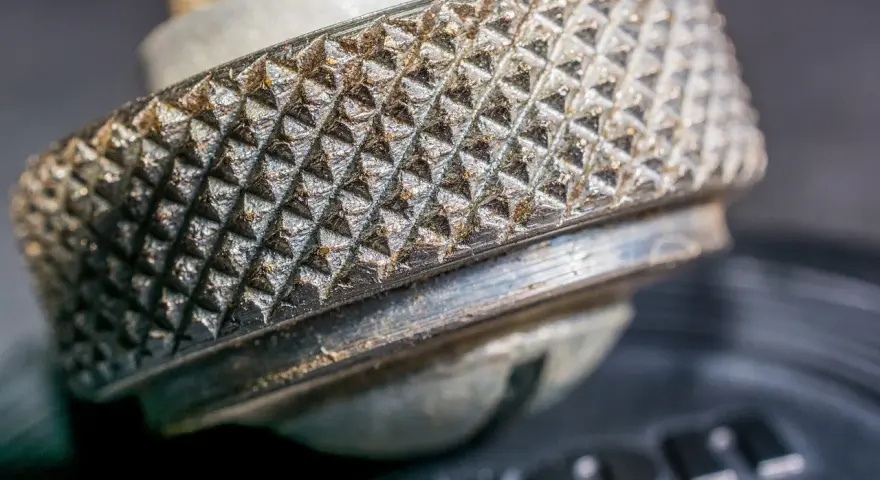 Zbliżenie na metalową nakrętkę z wyraźnym radełkowaniem, przypominającym rysunek techniczny.