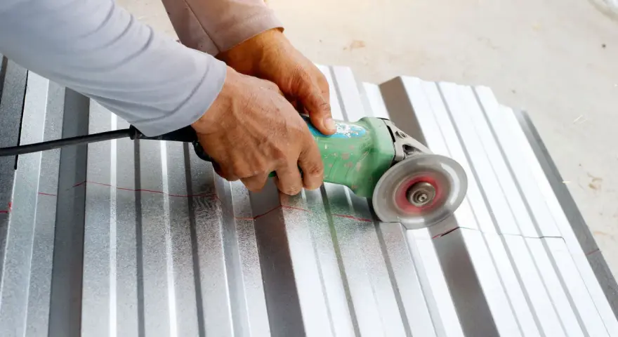 Ręce trzymają szlifierkę kątową, którą tnie się blachę aluminiową wzdłuż czerwonej linii.