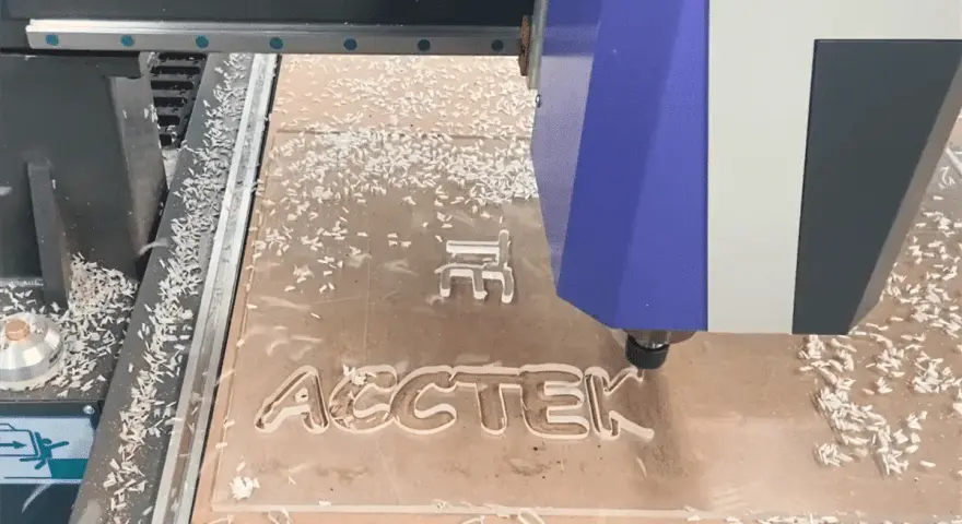 CNC frezuje napis "ACCTEК" na płycie, tworząc różne rodzaje wiórów.