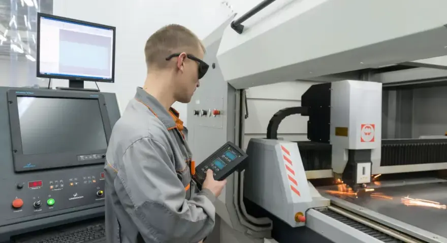 Operator CNC w okularach ochronnych steruje maszyną laserową, która precyzyjnie tnie metal.