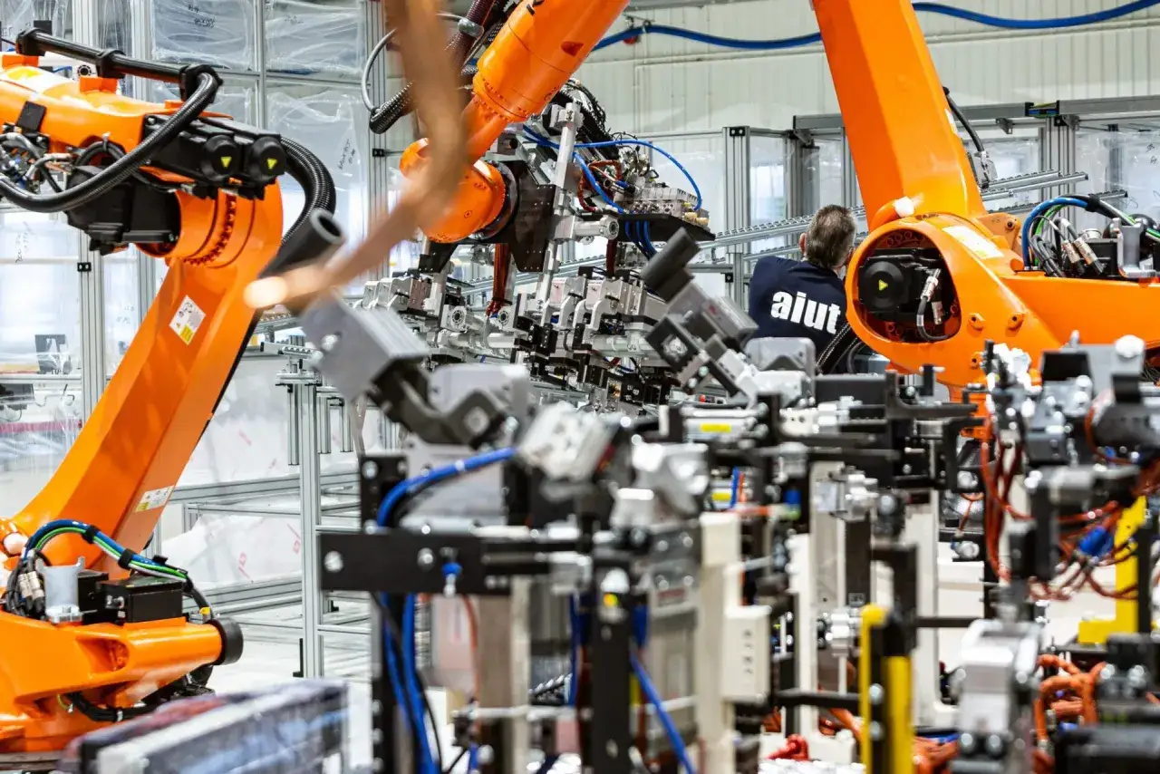 Pomarańczowe ramiona robotów pracują w fabryce, gdzie system MES zarządza produkcją.