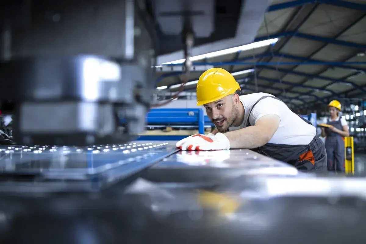 Pracownik w żółtym kasku i rękawicach dba o precyzyjną obsługę maszyn CNC, kontrolując proces produkcji metalowych elementów.