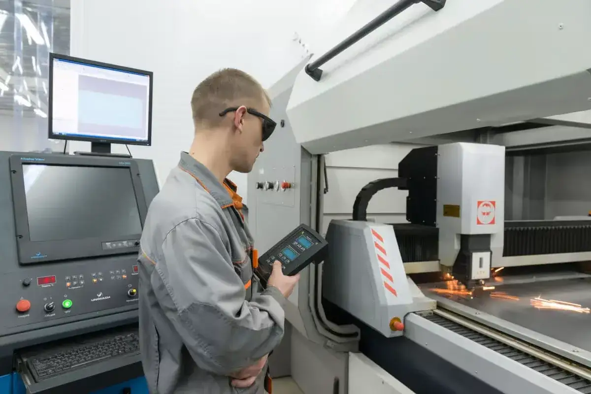 Operator CNC w okularach ochronnych steruje maszyną laserową, która precyzyjnie tnie metal.