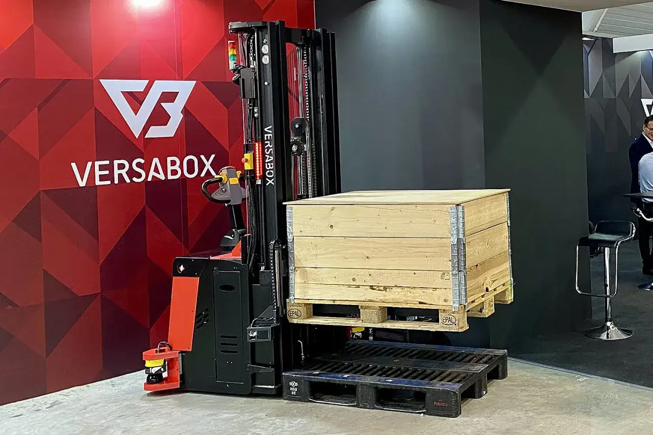 Autonomiczny wózek AGV Versabox podnosi drewnianą skrzynię z palety.