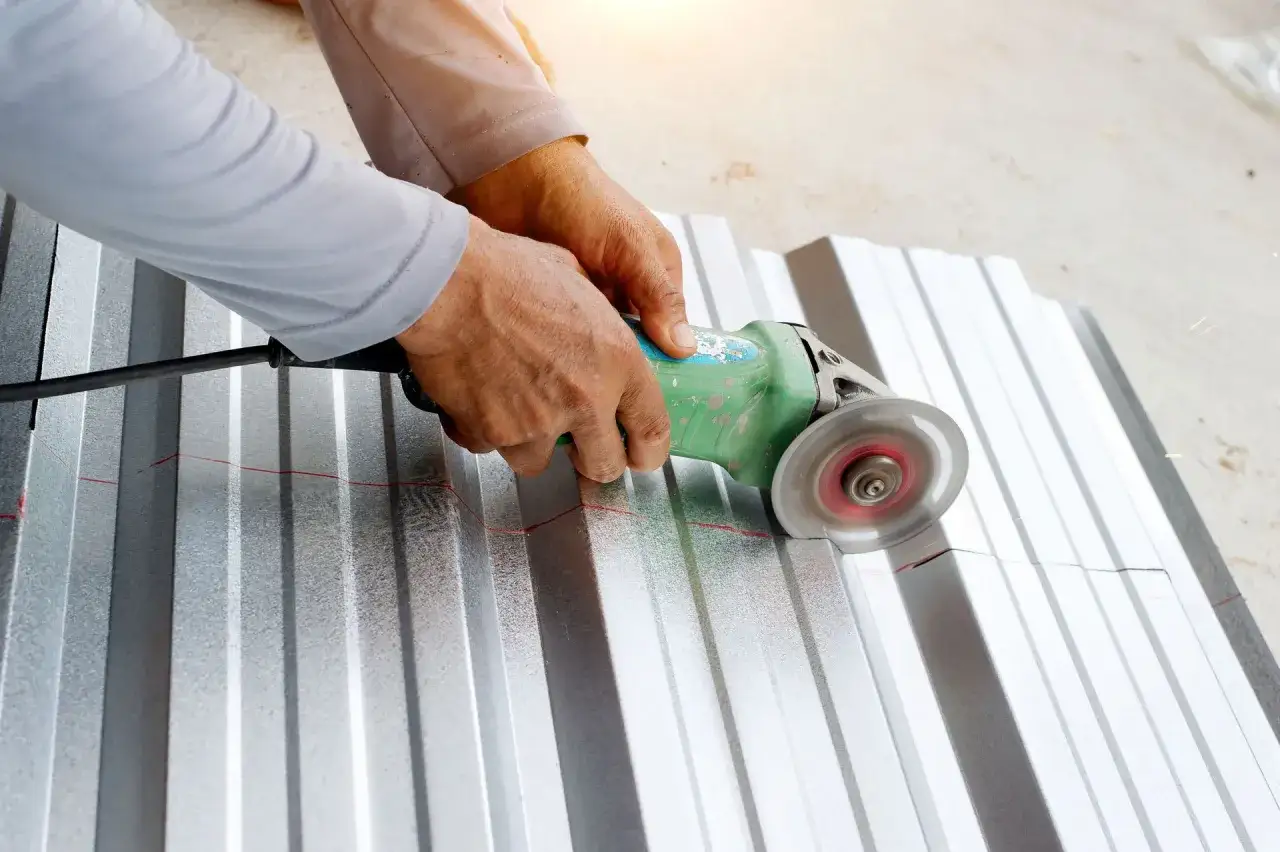 Ręce trzymają szlifierkę kątową, która tnie falistą blachę aluminiową wzdłuż czerwonej linii. To pokazuje, czym ciąć aluminium.