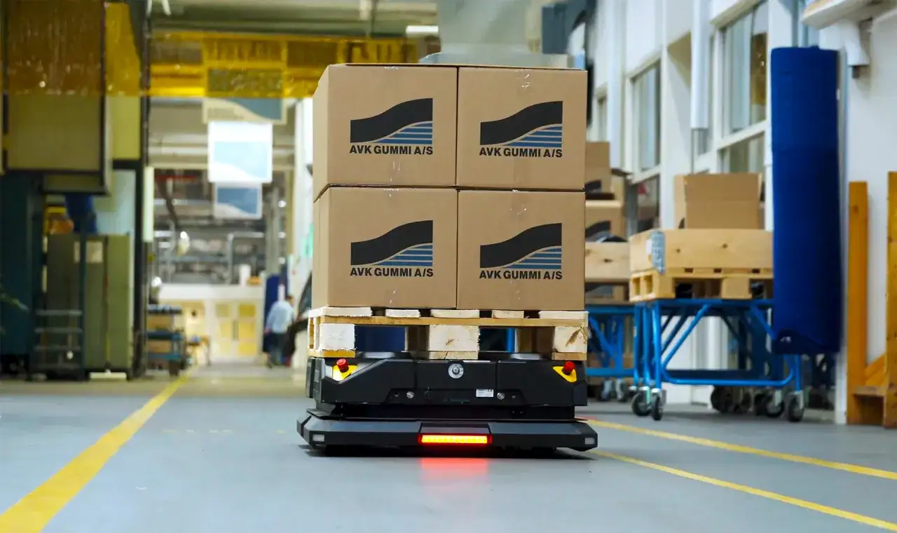 Autonomiczny wózek transportowy z czterema kartonami AVK GUMMI A/S na palecie. To przyszłość automatyzacji transportu w magazynie.